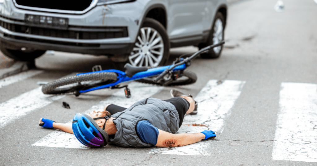 A cyclist lies on the ground, appearing injured after being struck by a car on a city street.