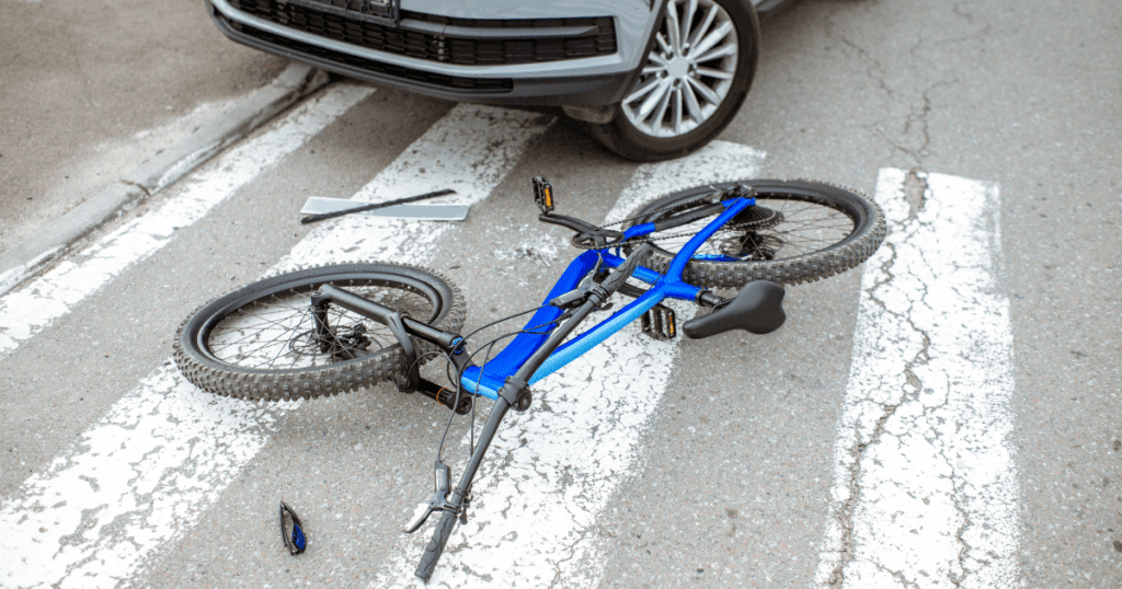 A bicycle lies on the ground next to a car, symbolizing a bike-car accident.