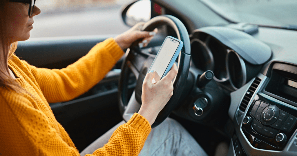 A woman is distractedly using her cell phone while driving a car on a busy road.